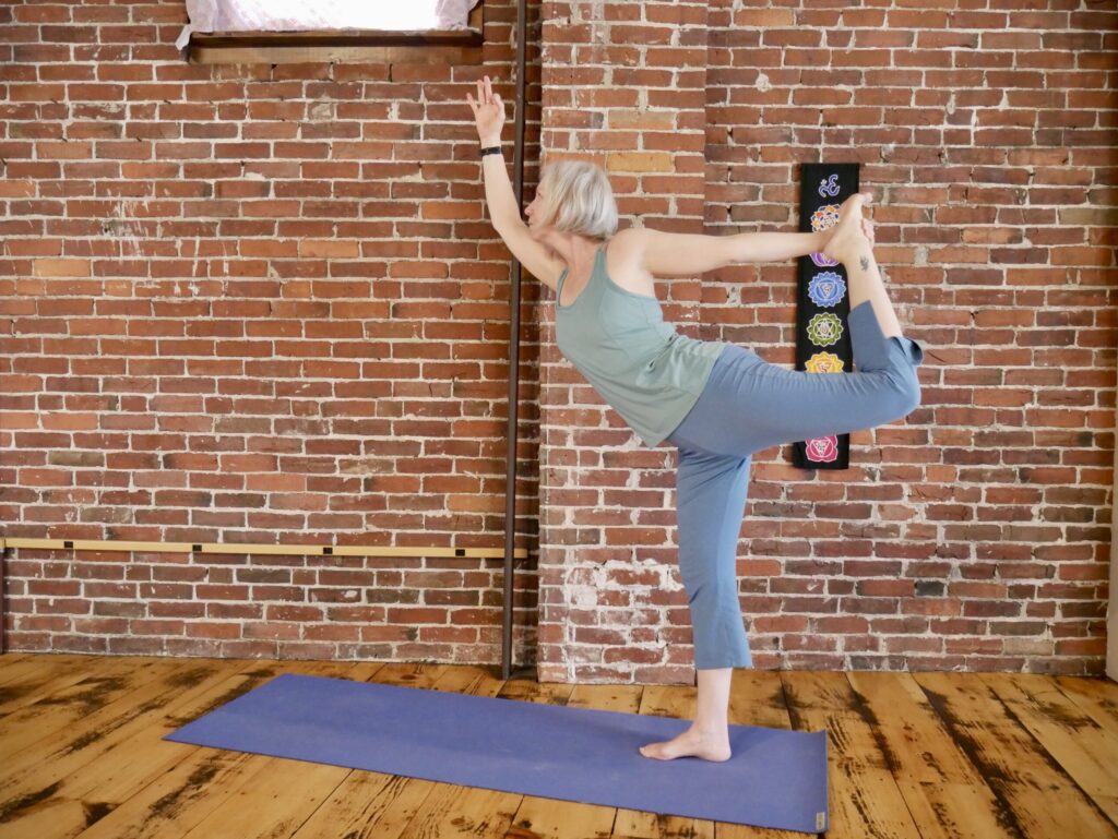 a woman in a standing yoga post on a mat, holding her foot with one arm in the air